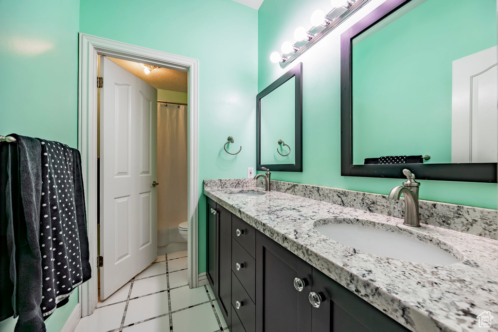 Bathroom with toilet, dual bowl vanity, and tile patterned floors