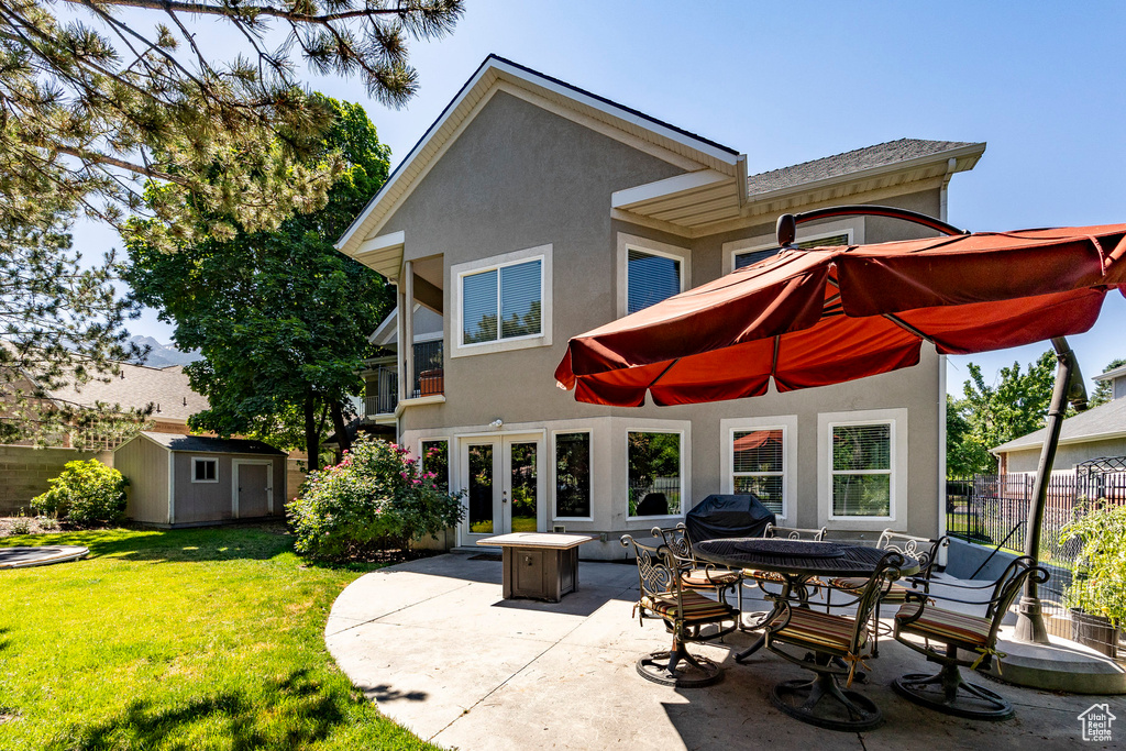 Rear view of property featuring a lawn, a patio, and a shed