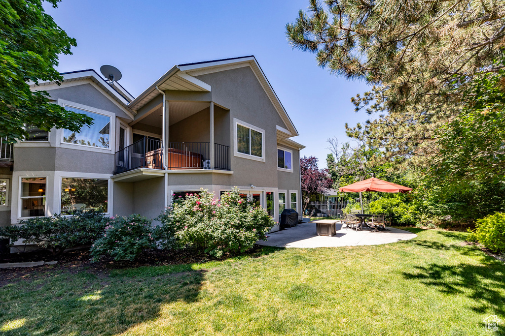 Back of property featuring a balcony, a lawn, and a patio area