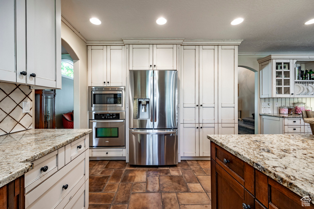 Kitchen with appliances with stainless steel finishes, dark tile patterned floors, decorative backsplash, and white cabinets