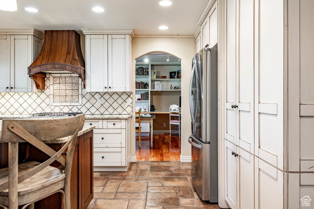 Kitchen featuring light tile patterned flooring, stainless steel refrigerator, decorative backsplash, and custom range hood