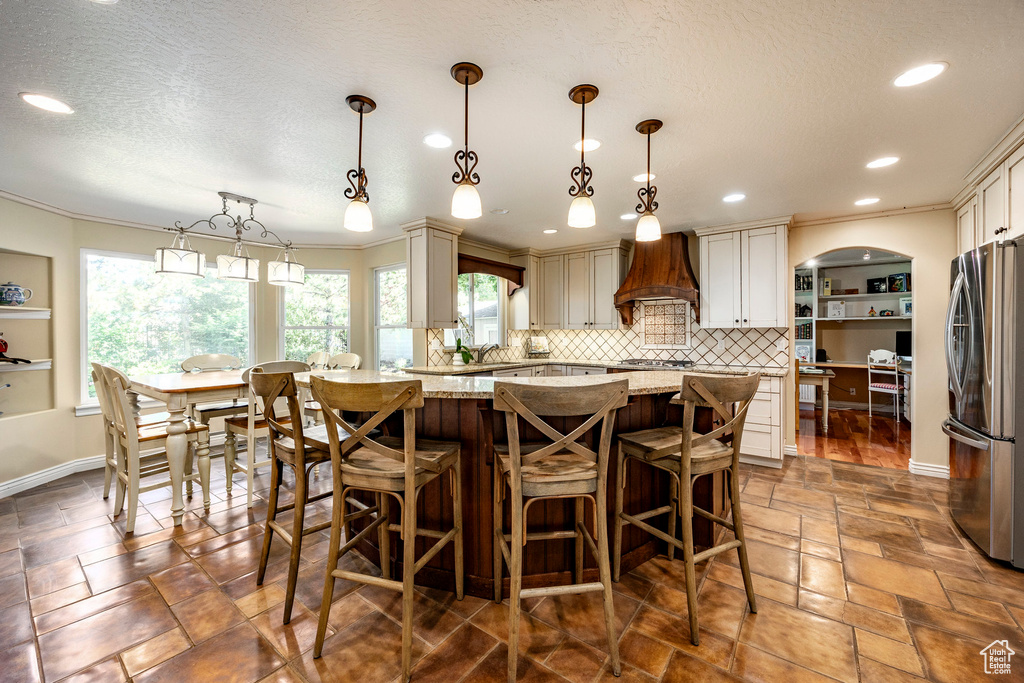 Kitchen featuring stainless steel fridge, plenty of natural light, tile patterned flooring, and premium range hood