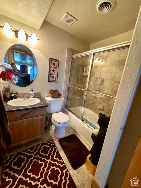 Full bathroom featuring vanity, combined bath / shower with glass door, tile patterned flooring, and toilet