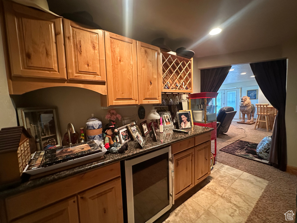 Kitchen with dark stone countertops, light colored carpet, and beverage cooler