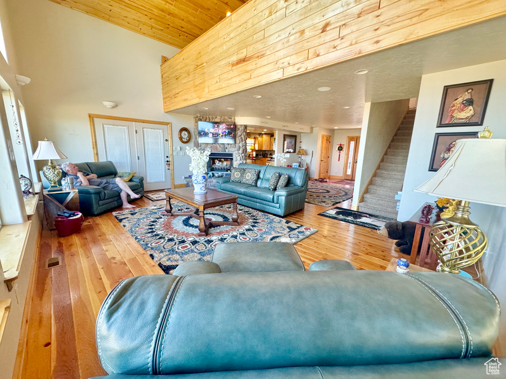 Living room featuring wood ceiling, a stone fireplace, hardwood / wood-style floors, and high vaulted ceiling