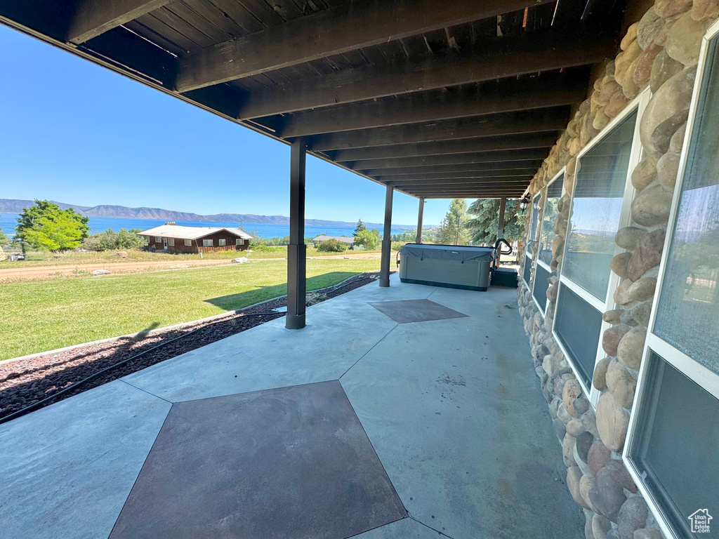 View of patio with a water view and a hot tub