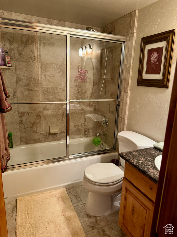 Full bathroom with tile patterned floors, toilet, enclosed tub / shower combo, and vanity