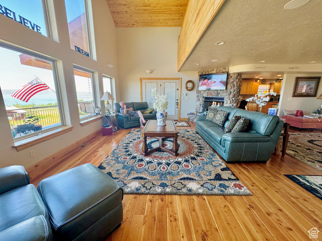 Living room featuring wood-type flooring, a high ceiling, wooden ceiling, a textured ceiling, and a stone fireplace