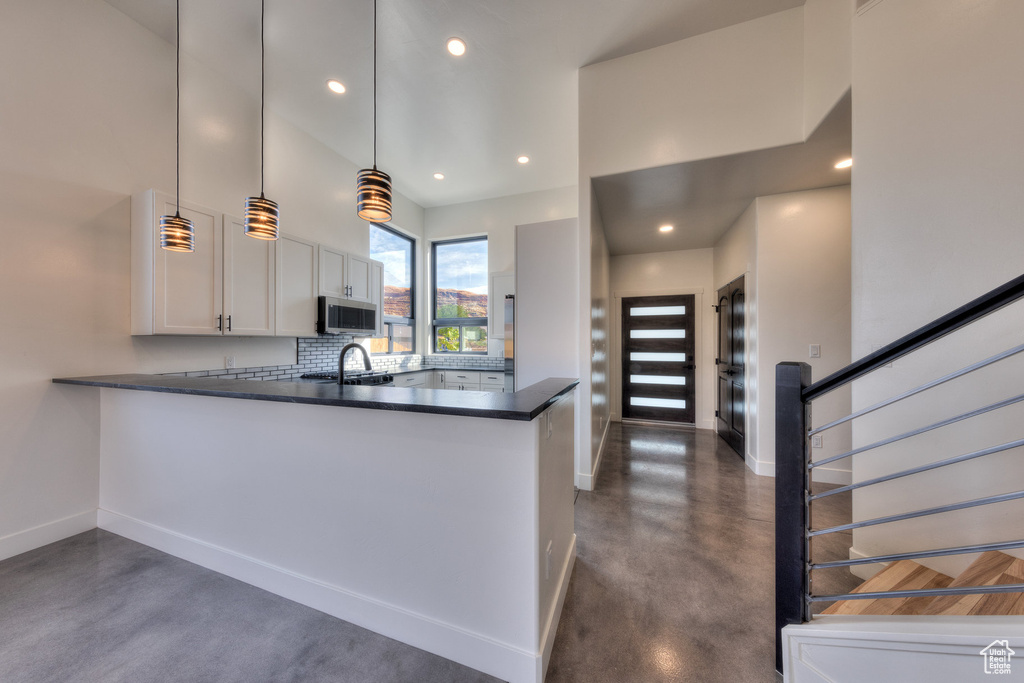 Kitchen featuring hanging light fixtures, kitchen peninsula, backsplash, and white cabinetry