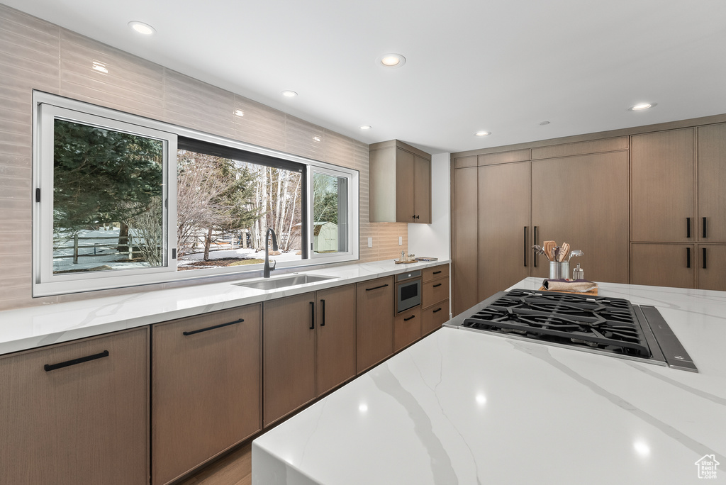 Kitchen featuring stainless steel gas stovetop, backsplash, light stone counters, built in microwave, and sink