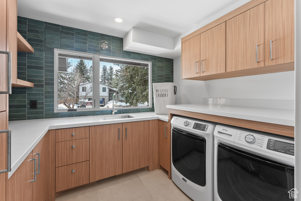 Laundry area featuring washing machine and clothes dryer, sink, and cabinets