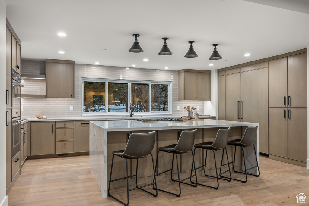 Kitchen with pendant lighting, a center island, decorative backsplash, and light wood-type flooring