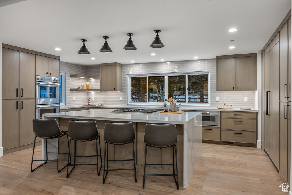 Kitchen with a kitchen island, light hardwood / wood-style flooring, stainless steel appliances, and tasteful backsplash