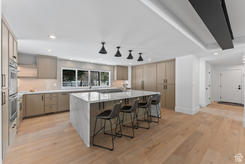 Kitchen featuring a breakfast bar area, light wood-type flooring, backsplash, and an island with sink