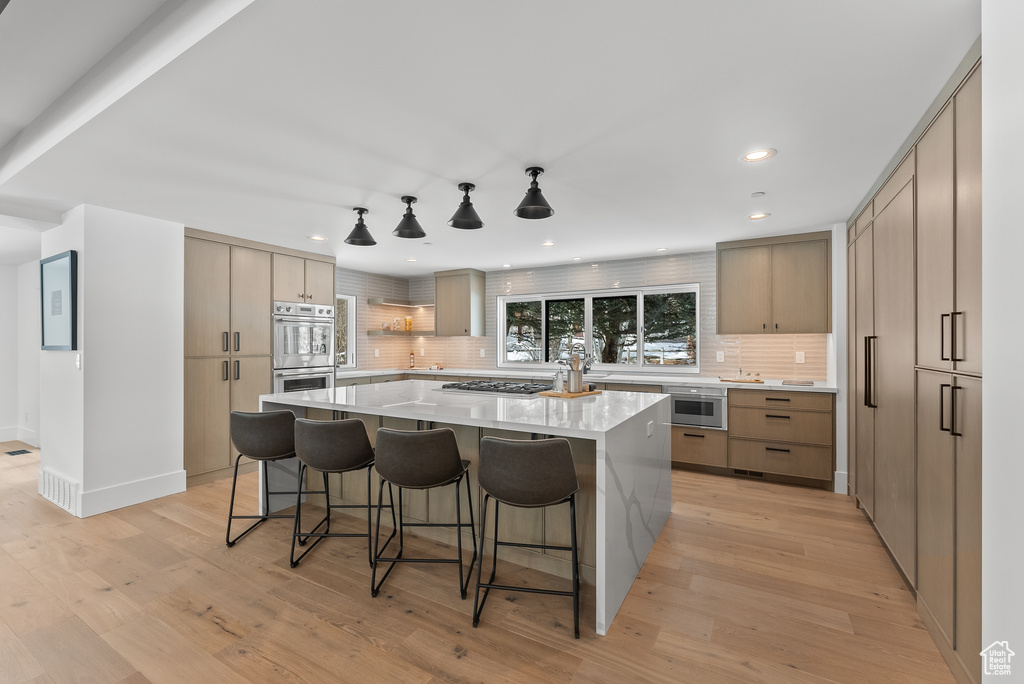 Kitchen featuring a kitchen breakfast bar, a center island, decorative backsplash, and light wood-type flooring