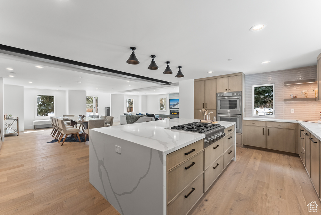 Kitchen with tasteful backsplash, light stone counters, a kitchen island, light hardwood / wood-style floors, and appliances with stainless steel finishes