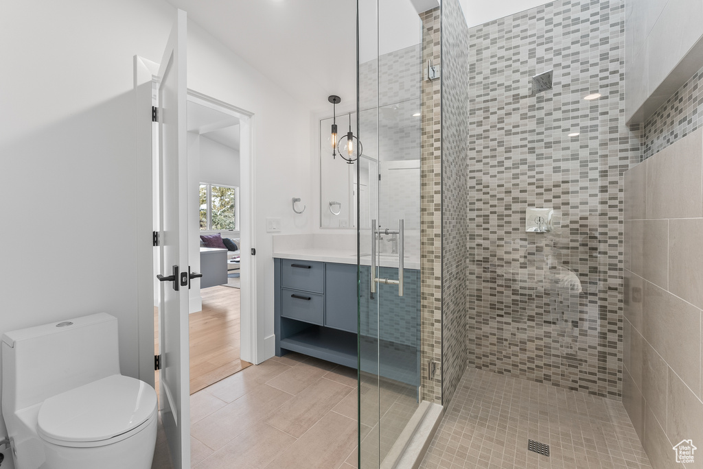 Bathroom featuring vanity, wood-type flooring, vaulted ceiling, toilet, and a shower with door