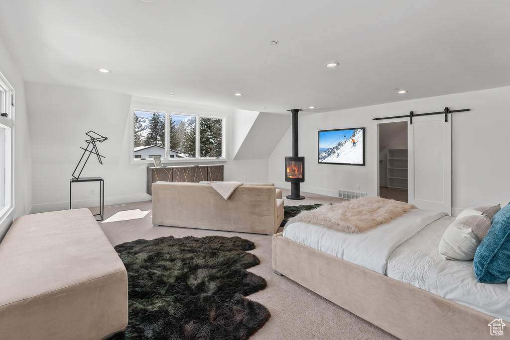 Bedroom with light carpet, a barn door, and a wood stove