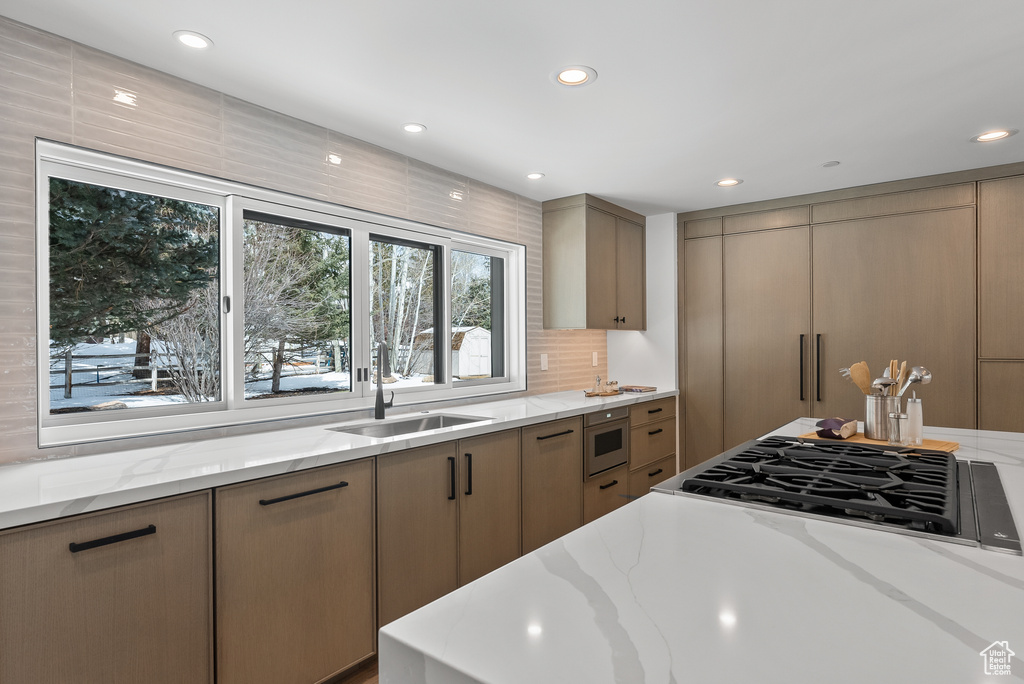 Kitchen with stainless steel gas cooktop, sink, light stone counters, and built in microwave