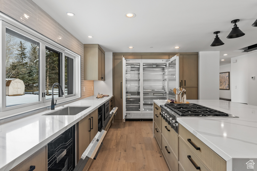 Kitchen with light brown cabinets, sink, stainless steel gas cooktop, light hardwood / wood-style floors, and backsplash