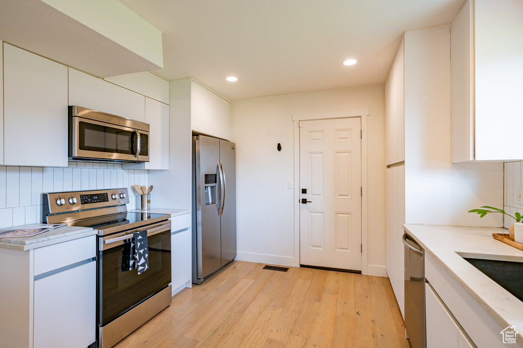 Kitchen featuring white cabinetry, stainless steel appliances, backsplash, and light hardwood / wood-style flooring