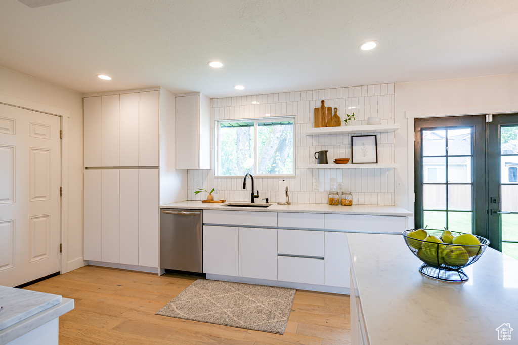 Kitchen featuring sink, dishwasher, light hardwood / wood-style flooring, and white cabinetry