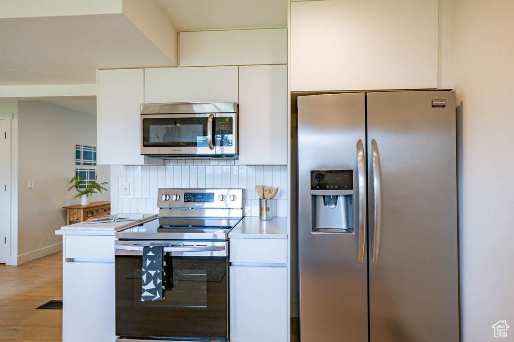 Kitchen featuring decorative backsplash, stainless steel appliances, light hardwood / wood-style floors, and white cabinetry