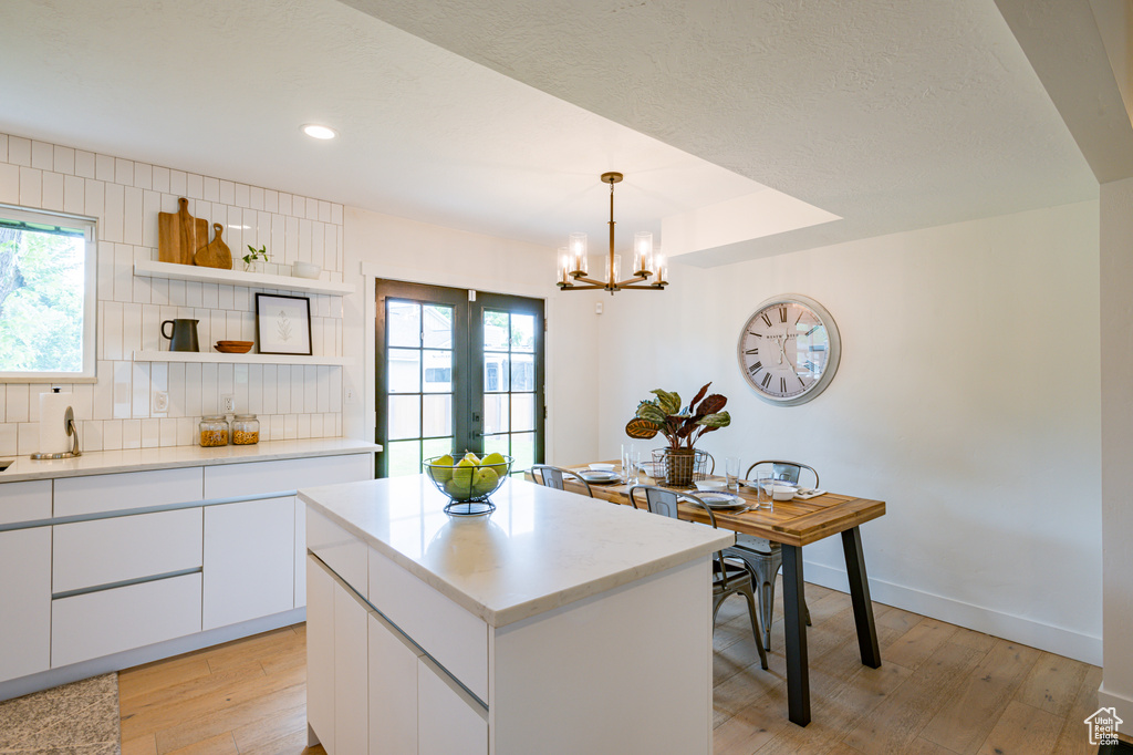 Kitchen featuring light hardwood / wood-style flooring, white cabinets, hanging light fixtures, a kitchen island, and decorative backsplash