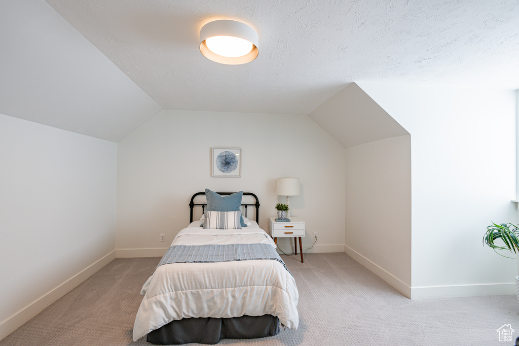 Carpeted bedroom featuring vaulted ceiling and a textured ceiling