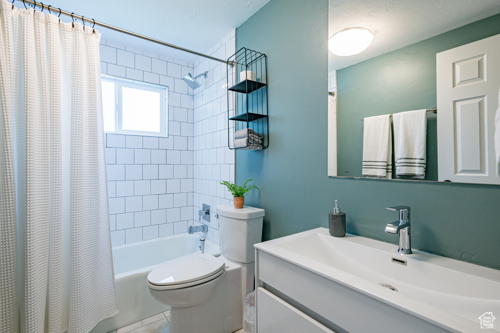 Full bathroom with shower / tub combo with curtain, vanity, tile patterned floors, toilet, and a textured ceiling