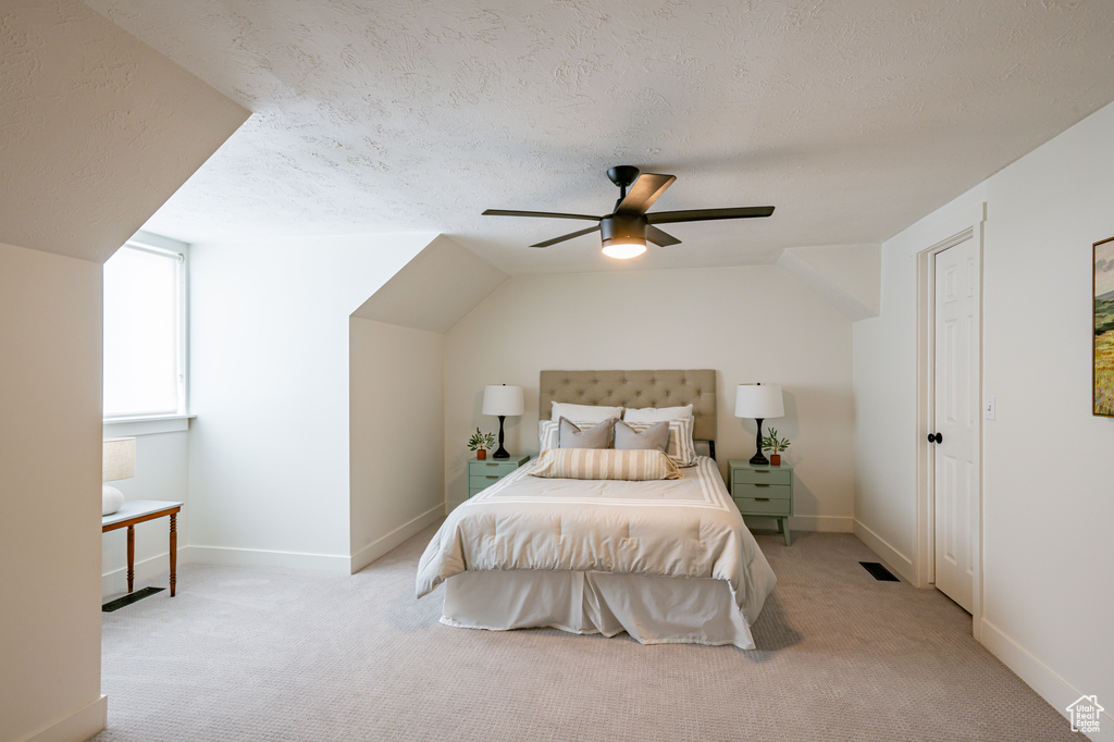 Bedroom featuring a textured ceiling, ceiling fan, vaulted ceiling, and light carpet