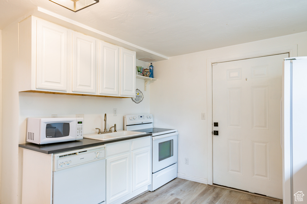 Kitchen featuring sink, white cabinets, light wood-type flooring, and white appliances