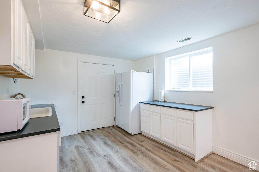 Kitchen with white cabinetry, light hardwood / wood-style flooring, white appliances, and sink