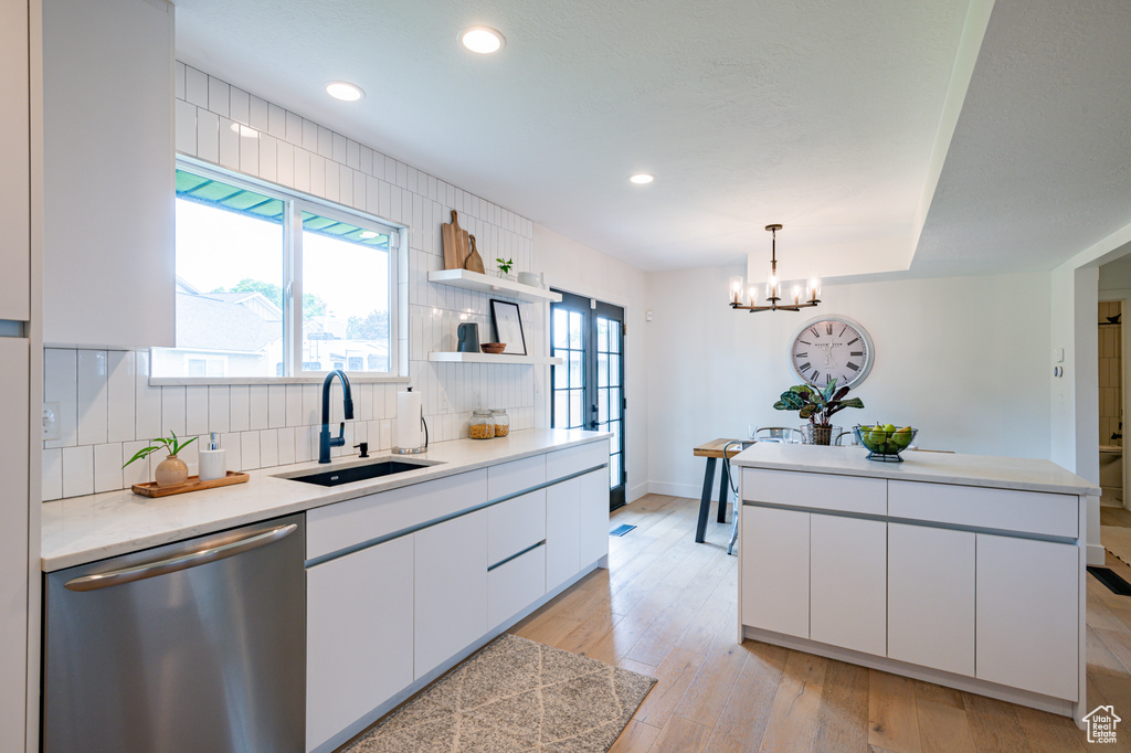 Kitchen with stainless steel dishwasher, sink, white cabinets, and light hardwood / wood-style floors