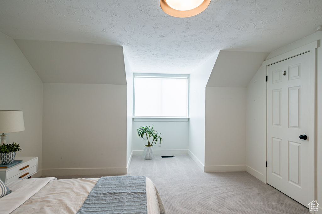 Bedroom featuring lofted ceiling, light carpet, and a textured ceiling