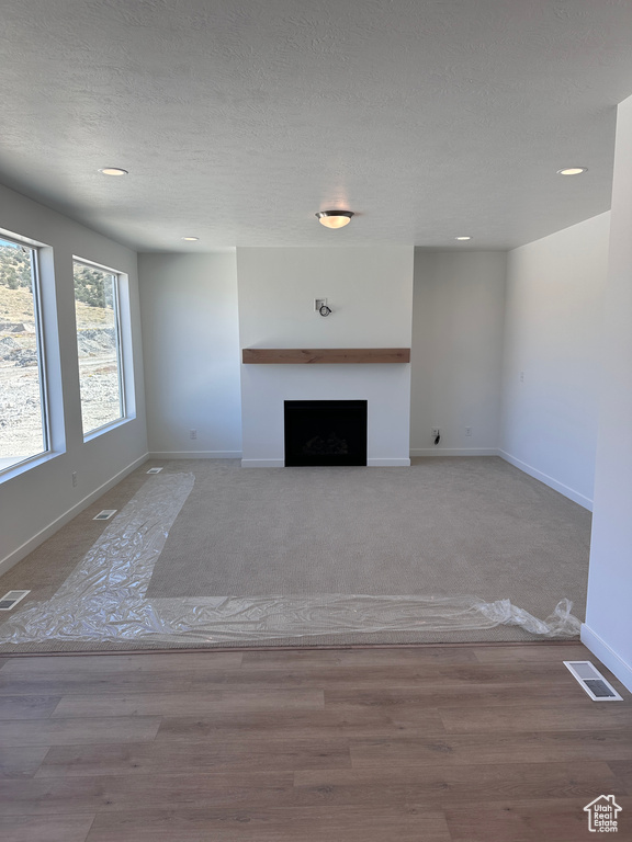 Unfurnished living room with light wood-type flooring and a textured ceiling