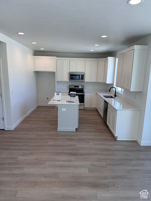 Kitchen featuring white cabinets, sink, light hardwood / wood-style flooring, stainless steel appliances, and a center island