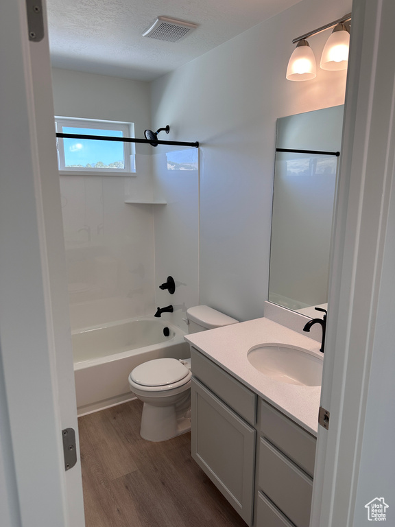 Full bathroom featuring vanity, a textured ceiling, washtub / shower combination, hardwood / wood-style floors, and toilet