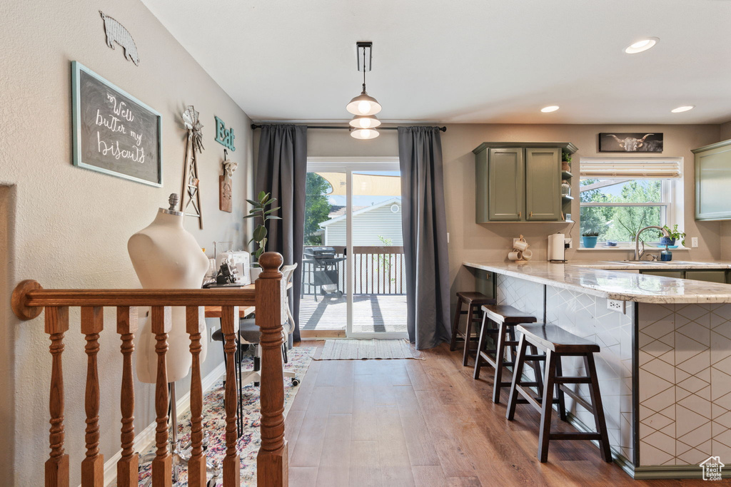 Kitchen with decorative light fixtures, a kitchen bar, light stone countertops, light hardwood / wood-style floors, and kitchen peninsula