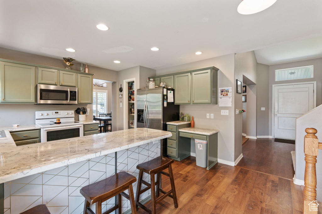 Kitchen with dark hardwood / wood-style flooring, appliances with stainless steel finishes, green cabinetry, kitchen peninsula, and a kitchen breakfast bar