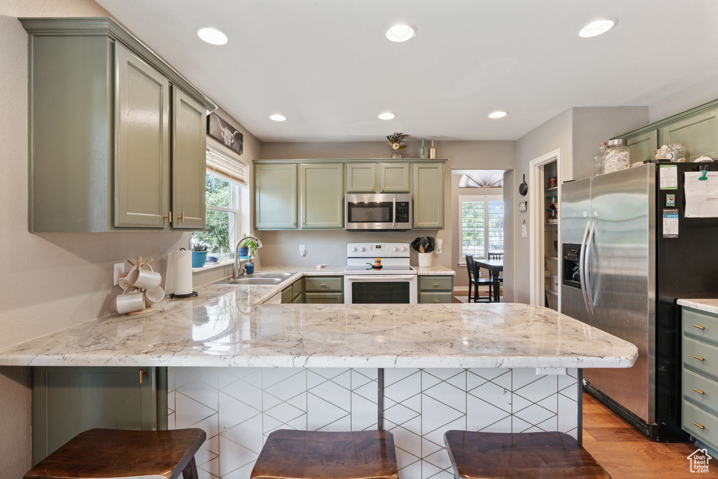 Kitchen featuring stainless steel appliances, sink, light hardwood / wood-style floors, kitchen peninsula, and a kitchen breakfast bar