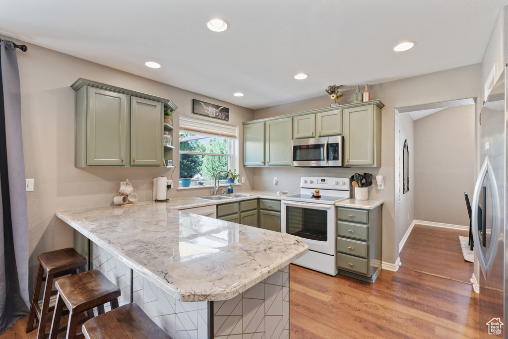 Kitchen with a breakfast bar area, white range with electric cooktop, kitchen peninsula, light hardwood / wood-style floors, and sink