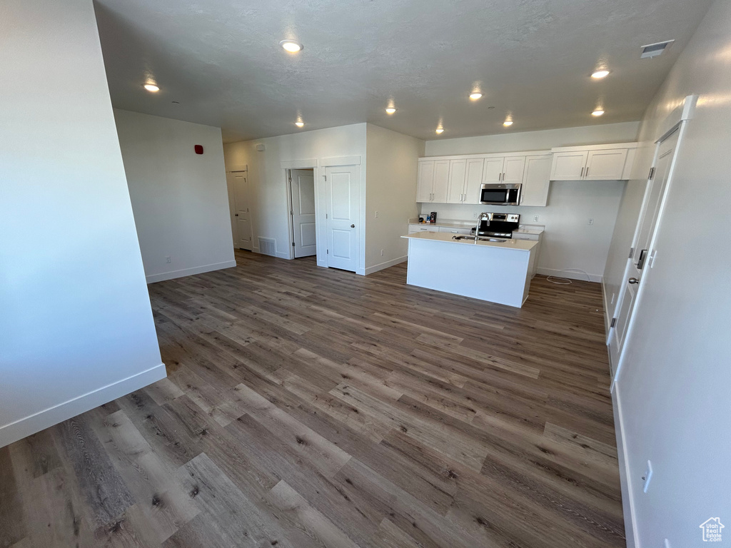 Kitchen with white cabinetry, wood-type flooring, an island with sink, and stainless steel appliances
