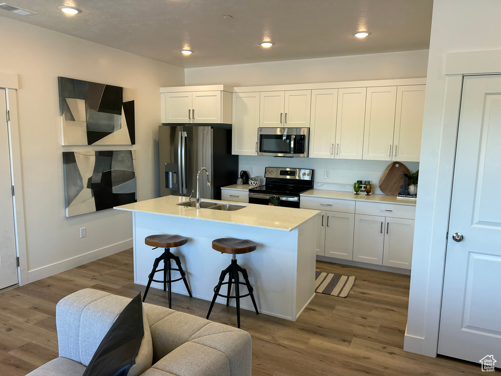 Kitchen featuring white cabinets, stainless steel appliances, and an island with sink