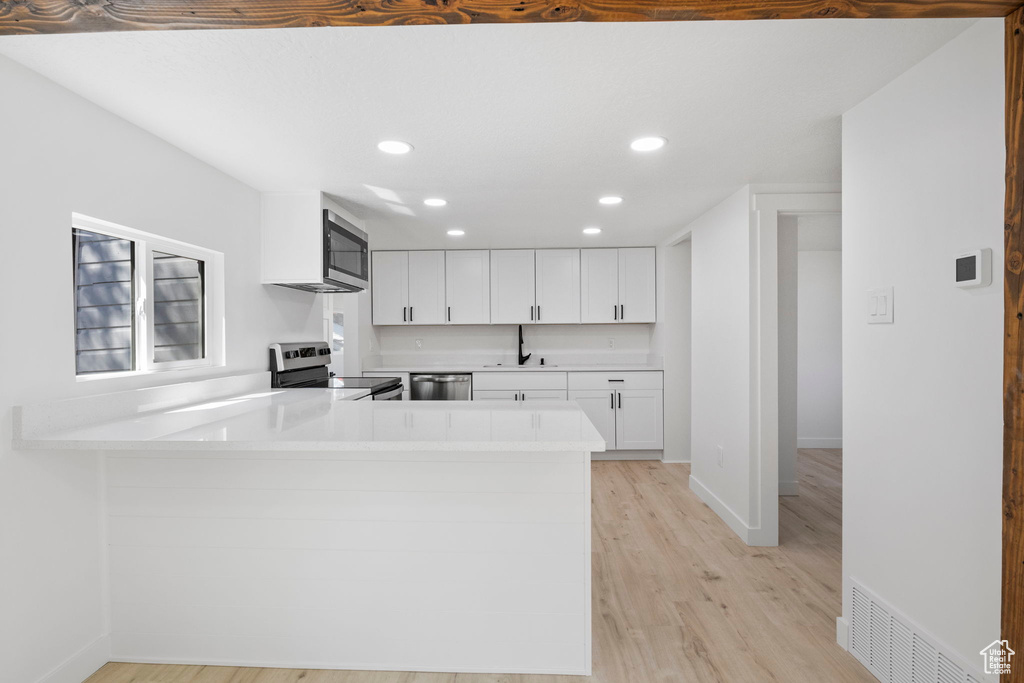 Kitchen featuring appliances with stainless steel finishes, white cabinets, sink, kitchen peninsula, and light hardwood / wood-style floors