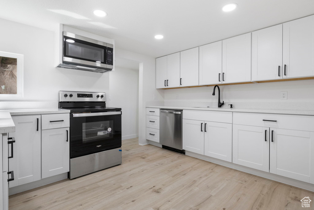 Kitchen with sink, appliances with stainless steel finishes, light wood-type flooring, and white cabinets