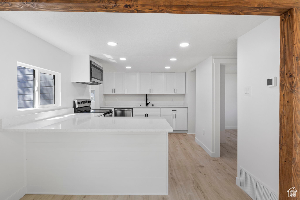 Kitchen with white cabinetry, kitchen peninsula, stainless steel appliances, light hardwood / wood-style floors, and sink