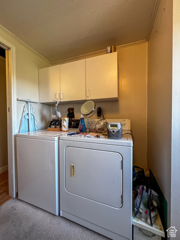 Laundry room with washer and clothes dryer, light carpet, cabinets, and ornamental molding