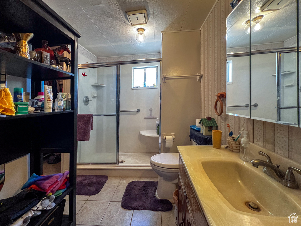 Bathroom with vanity, toilet, a shower with door, a textured ceiling, and tile patterned flooring