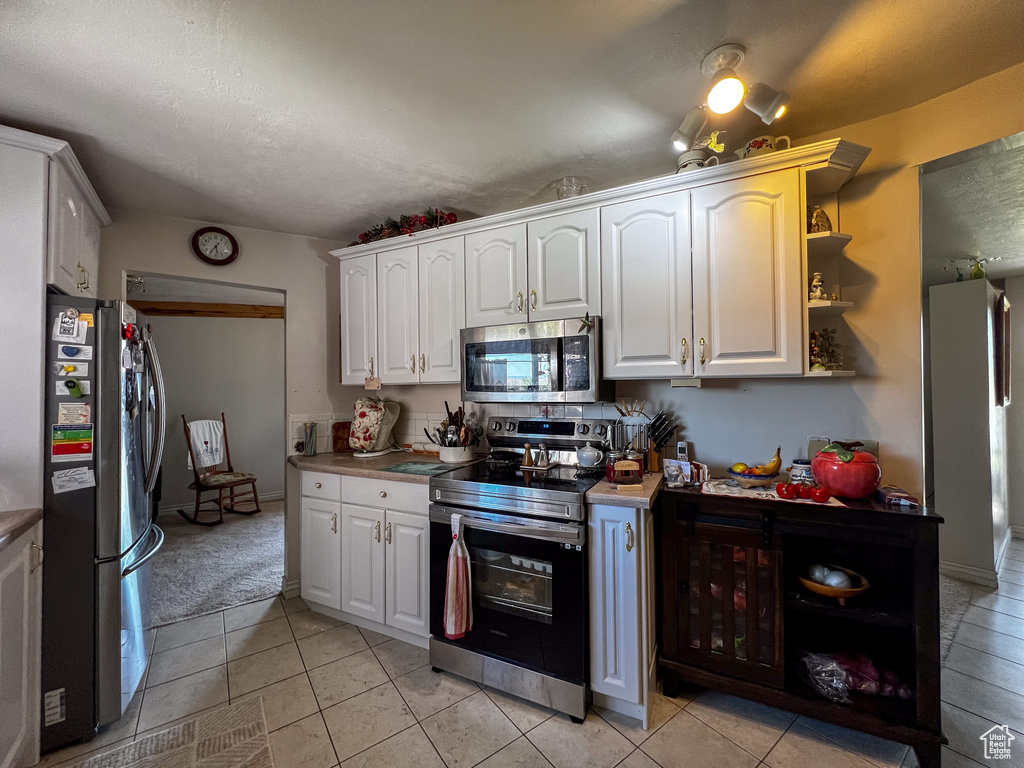 Kitchen with appliances with stainless steel finishes, light tile patterned floors, and white cabinets